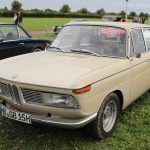 Cremefarbene BMW-Limousine der Neuen Klasse auf einer Wiese